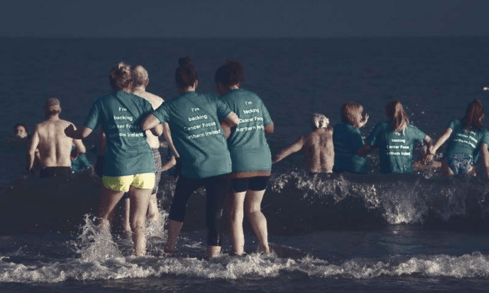 people in cancer focus ni t-shirts running into water in dark