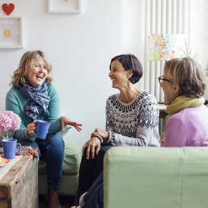 Mature women friends and sisters sitting together in a living room in Cornwall talking together.